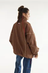 Campera rompevientos beige de nylon con diseño oversize, cuello alto, cierre frontal negro y detalles de costuras y ribetes en contraste.