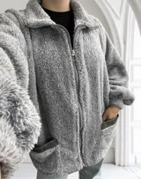 Camperón gris de tela tipo peluche con cierre frontal y bolsillos laterales.