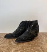 Botinetas negras de cuero con punta fina, cierre lateral y tachas plateadas.