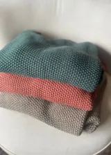 Buzo tejido en punto arroz de color terracota con hilo de lurex dorado, cuello redondo y detalle de flecos en los puños. Diseño holgado de manga larga.