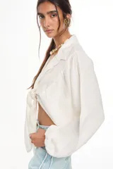 Top corto de lino italiano con diseño a cuadros en tonos verde oliva, beige y rosado, cuello camisero, mangas largas abullonadas con puños elásticos y nudo frontal ajustable.