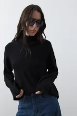 Polera de tejido liviano en color negro, con cuello alto, mangas largas y corte relajado. Presenta un diseño minimalista con recortes laterales que aportan estructura a la prenda.
