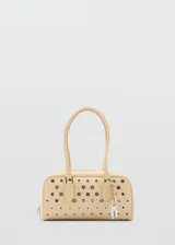 Bolso tipo bowling de color beige, adornado con múltiples ojales metálicos plateados en la parte frontal. Cuenta con doble asa de mano superior y cierre con cremallera.