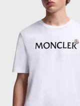 Remera de algodón blanca de corte clásico, con cuello redondo y mangas cortas. Presenta el nombre de la marca estampado en el frente en color negro, acompañado por el logo icónico de la marca en pequeño.