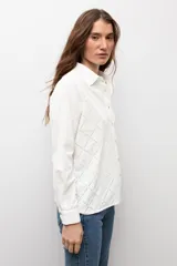 Camisa blanca de manga larga con frente de tela broderie con diseño de rombos calados y espalda lisa. Presenta cuello clásico y cierre frontal con botones.