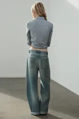 Jeans de tiro medio con cinco bolsillos, trabillas y cierre frontal con cremallera y botón metálico. Presenta un diseño baggy con piernas anchas, roturas decorativas y dobladillo vuelto en los bajos.