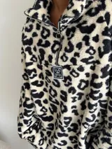 Buzo de peluche con estampado animal print, cuello alto con cierre frontal parcial y detalle de etiqueta decorativa en el pecho.
