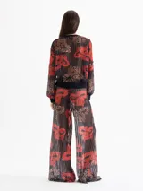 Pantalón Lexi de punto calado con estampado full print en tonos rojos, negros y marrones. Tiene cintura elastizada y bota amplia.