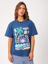 Remera azul de manga corta, corte holgado y cuello redondo, con estampado frontal colorido de temática tropical que incluye una palmera, un sol, flores y texto.