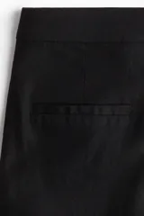 Pantalón sastrero de tiro alto y pierna ancha, confeccionado en una mezcla liviana de lino y viscosa. Presenta un diseño tobillero con cierre frontal, pretina con botón, pliegues marcados en la parte delantera y trasera, bolsillos laterales al bies y bolsillos decorativos en la parte posterior.