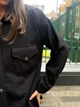 Camisa de estilo western en color negro, confeccionada en tejido de textura sutil. Presenta cuello clásico, cierre frontal con botones, dos bolsillos delanteros con solapa y costuras decorativas en el canesú que definen su diseño característico.