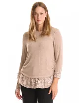 Buzo de tejido fino color beige con diseño de doble capa que simula una camisa debajo. Presenta cuello redondo, mangas largas con puños de gasa estampada en animal print, y ruedo con volado de la misma tela. Incluye detalles de frunces en los laterales.