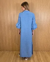 Vestido largo tipo túnica de color azul con estampado a cuadros blancos, cuello mao con escote en V y botones frontales parciales. Presenta mangas tres cuartos con volados en cascada.