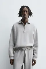 Polo de punto de corte relajado, confeccionado en mezcla de algodón, con cuello solapa, cierre frontal de cremallera y manga larga con acabados en rib.