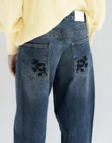 Jean wide leg de tiro medio, color azul con lavado denim, con bolsillos traseros decorados con una estampa floral oscura.