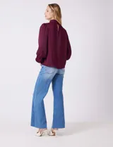 Blusa Tahari de gasa satén color violeta oscuro, con cuello alto fruncido y mangas largas abullonadas. La espalda tiene una abertura central con cierre de botón.