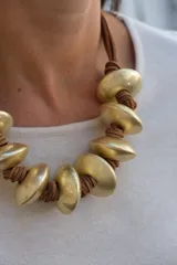 Collar de diseño artesanal compuesto por piezas circulares de metal dorado con acabado mate, intercaladas con nudos de cordón de cuero marrón.