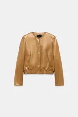 Campera bomber de cuero 100% color tostado de la ZARA WOMAN COLLECTION, con cuello redondo, manga larga, bolsillos delanteros ribeteados y cierre frontal con botones metálicos en relieve. Presenta elástico fruncido en el dobladillo inferior.