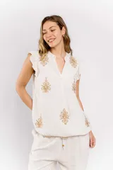 Blusa color crudo de lino con bordados dorados, cuello en V y mangas cortas con volados.