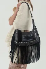 Cartera negra de cuero con textura croco y flecos largos de descarne agamuzado. Tiene detalles de tachas metálicas y correa larga desmontable para usar al hombro o cruzada.