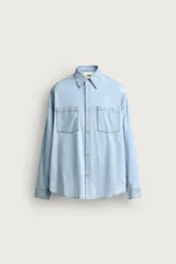 Camisa de corte relajado confeccionada en denim ligero de algodón, con cuello solapa, manga larga con puños abotonados y bolsillos de plastrón en el pecho. Presenta un acabado con efecto lavado y cierre frontal mediante botones.