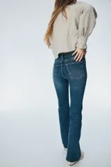 Jean de denim azul con tiro alto, cierre con botón y piernas amplias con bajos acampanados.