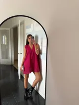 Vestido corto color fucsia, con escote en V profundo y mangas cortas tipo volado. Presenta un diseño con textura de bordado inglés o perforado y un corte imperio con frunce que da volumen a la falda.