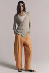Chaqueta de punto color beige con escote en V, manga larga y cierre frontal con botones dorados.