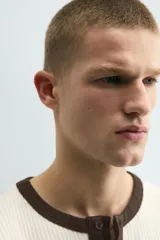 Camiseta de manga larga en tejido de punto canalé color crudo, con cuello redondo y tapeta frontal con botones en color marrón oscuro a contraste.