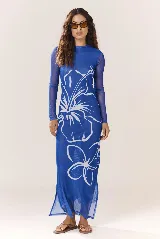 Vestido largo de malla azul traslúcida con estampado de flores blancas, cuello alto y mangas largas. Tiene aberturas laterales en el ruedo.