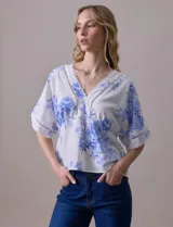 Blusa blanca estampada con flores azules, escote en V y mangas cortas amplias. Detalles de puntilla en escote y mangas.