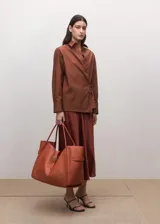 Camisa de algodón color marrón, de diseño cruzado estilo sobre con lazo lateral para anudar, cuello camisero, manga larga y calce amplio.