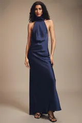 Vestido largo de satén azul marino con cuello halter y espalda descubierta. Presenta un cierre posterior con cremallera oculta y lazada en el cuello.