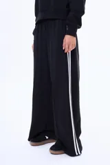 Pantalon de felpa color marrón con corte recto y holgado, presenta dos franjas blancas laterales a lo largo de cada pierna y cintura elástica.