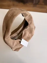 Cartera tipo hobo de diseño flexible y caída natural, confeccionada en material con textura simil gamuza. Cuenta con asa corta integrada para llevar al hombro, cierre superior y bolsillo interior con cierre.