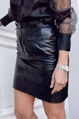 Minifalda negra de cuero, de corte a la cintura, con trabillas para cinturón y bolsillos delanteros ribeteados.