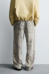 Pantalón de corte relajado confeccionado en tejido ligero de algodón con estampado abstracto de efecto lavado. Presenta cintura elástica, bolsillos frontales y bolsillos traseros de plastrón, con cierre frontal de cremallera y botón.
