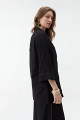 Blazer negro de corte recto y holgado, con doble botonadura frontal, solapas clásicas y mangas tres cuartos con costuras pespunteadas en contraste.