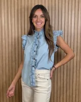 Musculosa de jean celeste sin mangas, con cuello alto fruncido, cierre frontal con botones y detalles de volados en las sisas y a lo largo de la botonera.