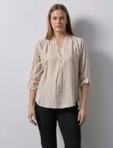 Blusa de manga larga con escote en V, confeccionada en tejido ligero con estampado de rayas verticales en tonos beige y blanco. Presenta un diseño con pliegue frontal y mangas ajustables mediante presilla y botón.