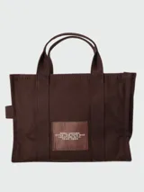 Bolso tipo tote de Marc Jacobs, confeccionado en lona resistente color beige. Presenta el logo estampado en contraste en el frente, doble asa superior y cierre superior con cremallera.