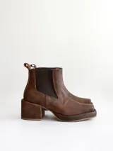 Bota tipo chelsea de cuero color chocolate con acabado texturizado, plataforma y taco cuadrado. Presenta paneles elásticos laterales en color negro.