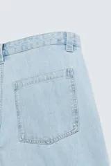 Shorts de denim de algodón, color celeste lavado, de corte regular fit y largo hasta la rodilla. Presenta cierre frontal con cremallera y botón, bolsillos delanteros y bolsillos traseros de plastrón. El borde inferior tiene un acabado deshilachado.