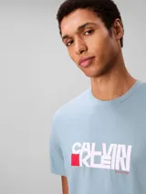 Remera Calvin Klein de color celeste, confeccionada en punto de algodón regenerativo, con cuello redondo, manga corta y corte regular. Presenta un estampado gráfico frontal con el logotipo de la marca en tonos blancos y un bloque rojo.