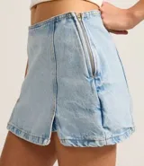 Short pollera de jeans celeste claro, tiro bajo, con ruedo deshilachado y un tajo lateral con detalle de encaje blanco en el borde.