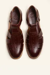 Sandalia cerrada tipo pescador de cuero negro charol, con tira en T y hebilla ajustable en el tobillo. Posee suela y taco bajo de madera.