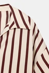 Camisa de cuello solapa con escote en pico, manga abullonada por debajo del codo con puños elásticos y diseño a rayas verticales.