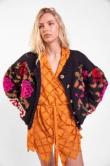 Cardigan de lana merino tejido y bordado a mano de calce holgado con cuello a la base, mangas largas y cierre frontal de botones. Presenta un diseño artesanal con bordados coloridos en las mangas y el cuerpo.