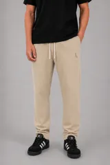 Pantalón tipo jogger color beige, con cintura elástica y cordón de ajuste. Presenta un pequeño bordado en la parte superior del muslo y puños elásticos en los tobillos.