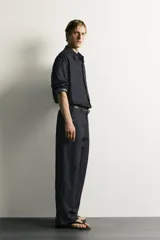 Pantalón chino para hombre confeccionado en denim ligero de mezcla de algodón y lino, sin lavados. Presenta un corte relajado con tiro medio, bolsillos frontales, bolsillos traseros y cierre frontal con cremallera y botón.